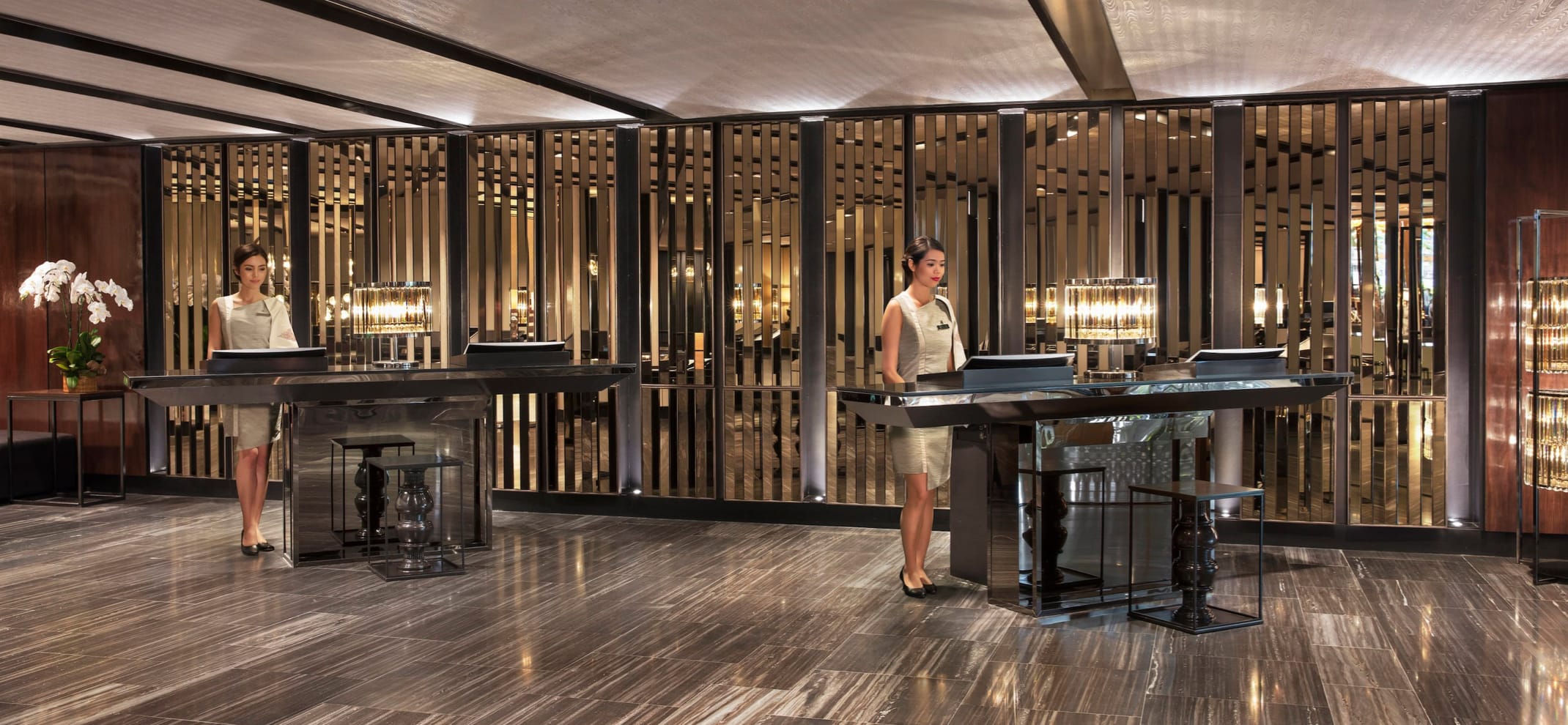 Two female concierges stand at sleek, minimalist concierge desks in a long hallway